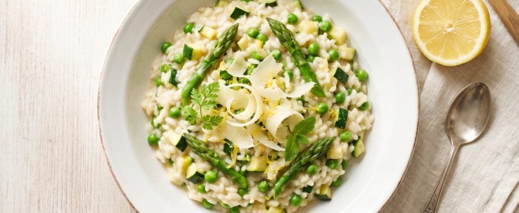 Creamy spring vegetable risotto with asparagus, peas, and zucchini topped with shaved Parmesan and lemon zest in a white bowl