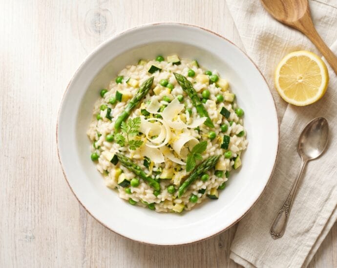 Creamy spring vegetable risotto with asparagus, peas, and zucchini topped with shaved Parmesan and lemon zest in a white bowl