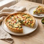 Garden vegetable quiche with zucchini, bell pepper, spinach and cheese in a golden crust, one slice removed