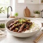 Instant Pot Mongolian beef with caramelized flank steak strips in a glossy soy glaze over white rice, topped with green onions and sesame seeds