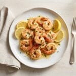 Garlic butter shrimp on a white plate with lemon wedges and parsley