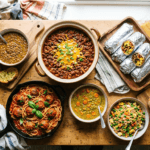 Overhead spread of budget friendly recipes including chili, lentil soup, spaghetti and meatballs and breakfast burritos